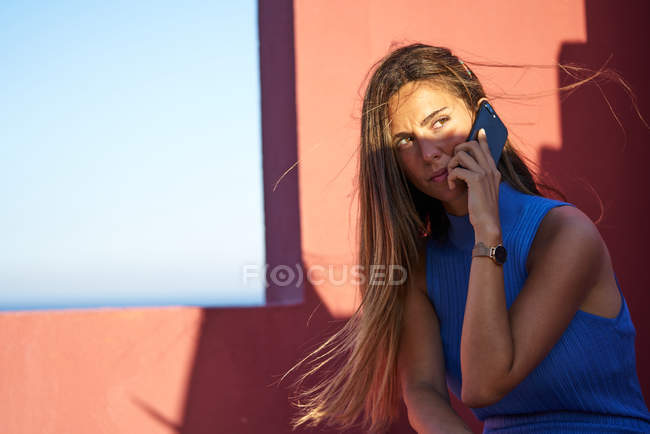 Bella donna felice seduta sul gradino del palazzo rosso e parlando con lo smartphone — Foto stock