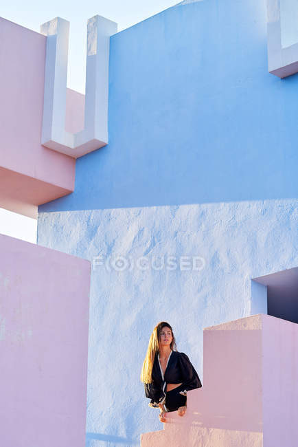 Femme debout sur le bâtiment pastel bleu et rose moderne et regardant loin — Photo de stock