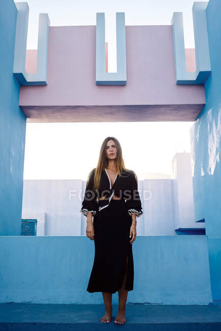 Barfuß steht eine schöne Frau auf einem modernen blauen Gebäude und blickt in die Kamera — Stockfoto
