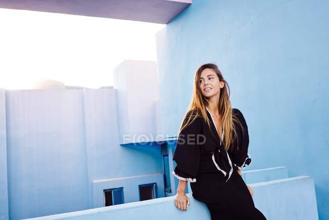 Schöne Frau lehnt an moderne blaue Wand Gebäude und schaut weg — Stockfoto