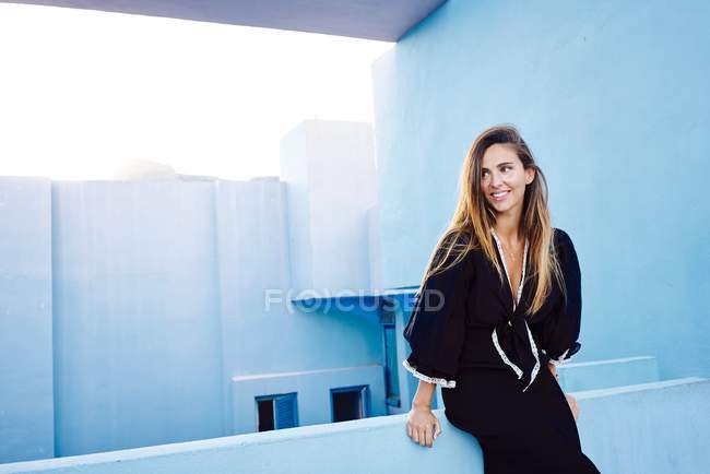 Mulher bonita apoiando-se no moderno edifício de parede azul e olhando para longe — Fotografia de Stock