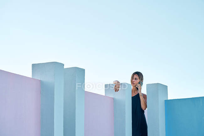 Mujer de pie en la parte superior del edificio azul y hablando por teléfono inteligente - foto de stock