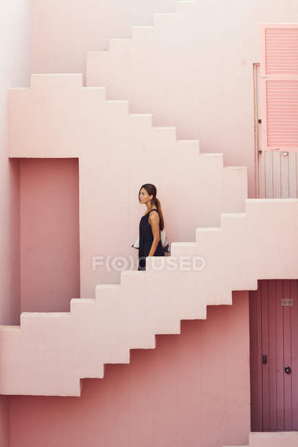Вид сбоку женщины, идущей вниз по современному розовому зданию — стоковое фото