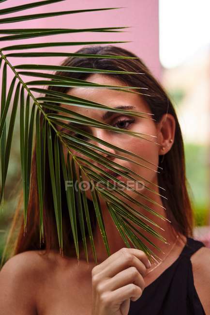 Close up of a beautiful woman looking at camera through palm tree leave — Stock Photo