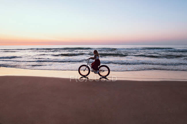 Радостная женщина на велосипеде вдоль спокойного пляжа — стоковое фото
