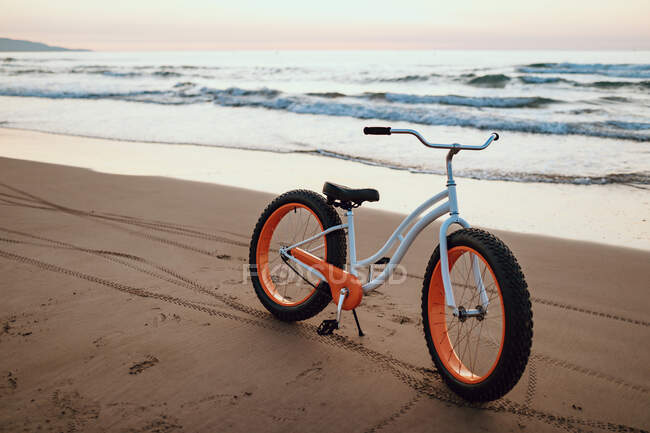 Moderna bicicleta gorda estacionada en la playa al atardecer - foto de stock
