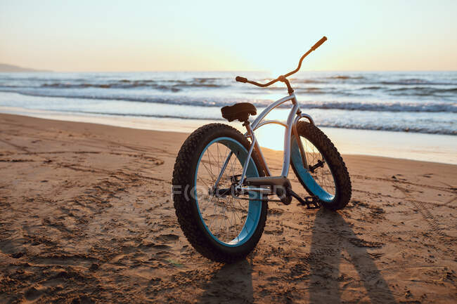 Блискучий новий жирний велосипед припаркований на піщаному спокійному узбережжі на літньому заході сонця — стокове фото