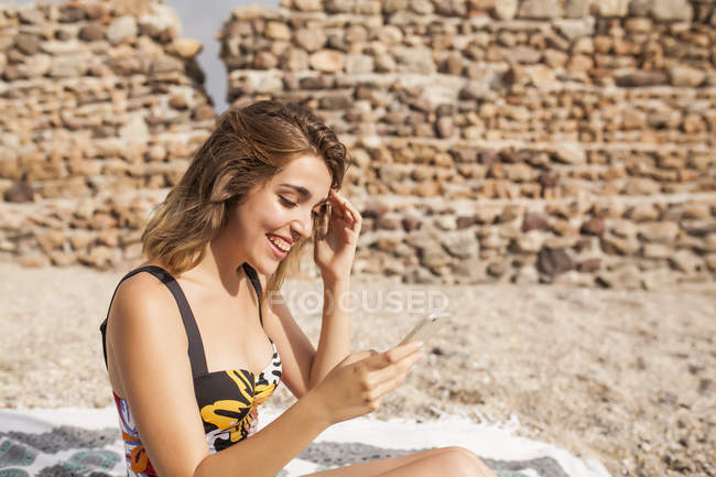 Молодая женщина в купальниках отдыхает на берегу моря и пользуется мобильным телефоном — стоковое фото