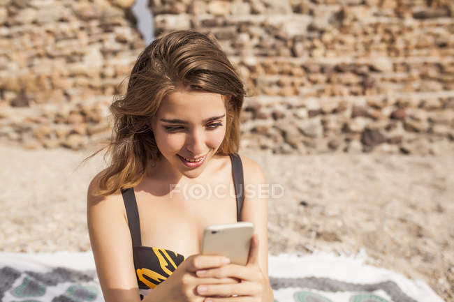 Young woman in swimwear relaxing on seashore and using mobile phone — Stock Photo