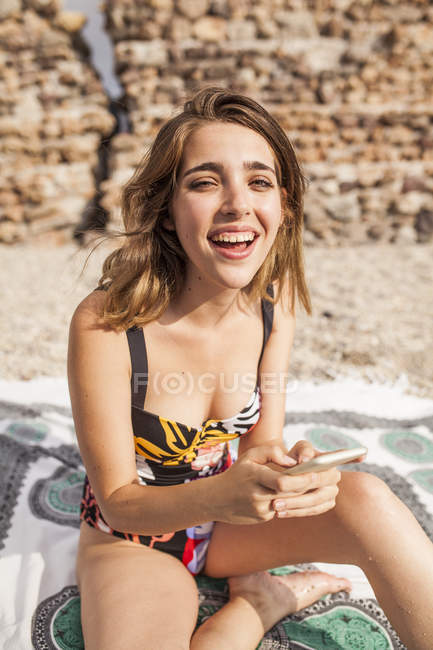 Jovem em roupa de banho relaxante na praia e usando telefone celular — Fotografia de Stock