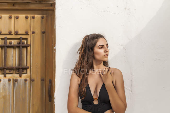 Красива жінка, дивлячись далеко, стоїть біля білої стіни в сонячний день — стокове фото