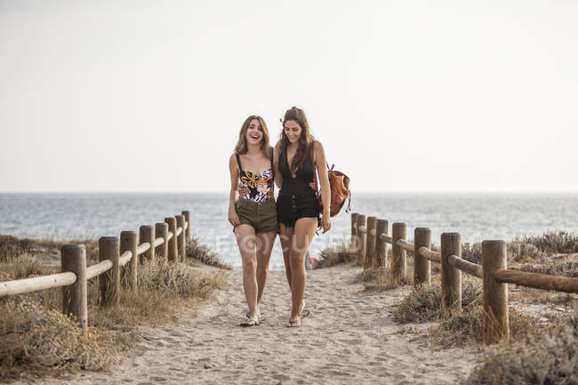 Frauen mit Rucksack gehen in der Nähe von Holzzaun, umarmen einander auf Natur Meeresküste Hintergrund — Stockfoto