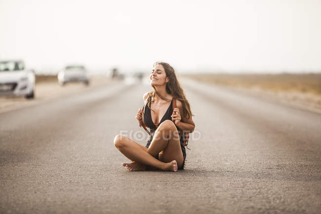 Приваблива молода жінка посміхається і сидить на дорозі з білими смужками — стокове фото