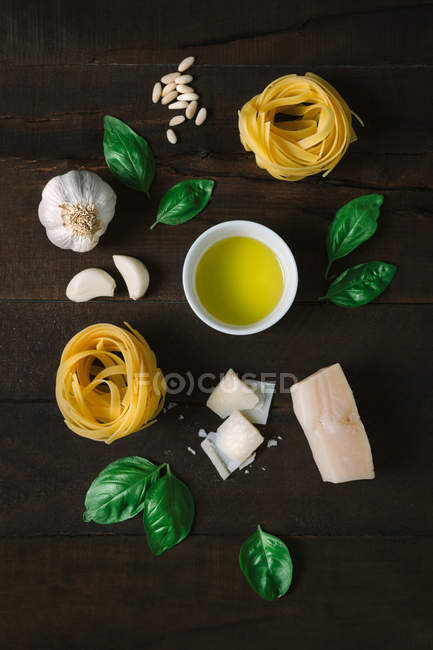 Vista superior de hierbas frescas y queso con aceite y pasta de tagliatelle dispuestas en la mesa rústica de madera. - foto de stock