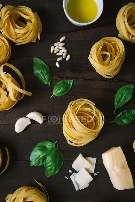 Raw tagliatelle pasta rolls with basil leaves, garlic and cheese on table — Stock Photo