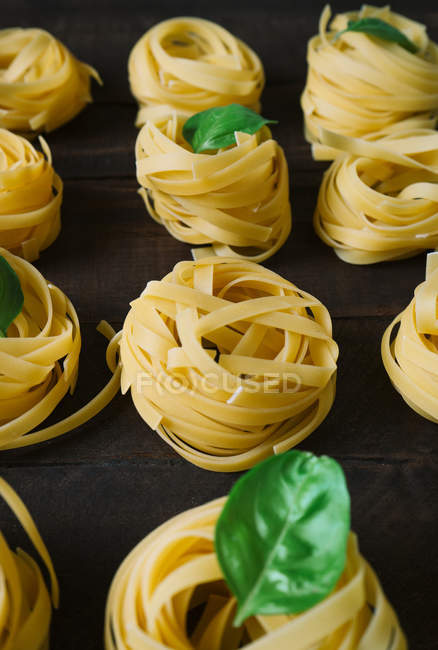 From above arranged pasta nests with fresh basil leaves on wooden kitchen table — Stock Photo