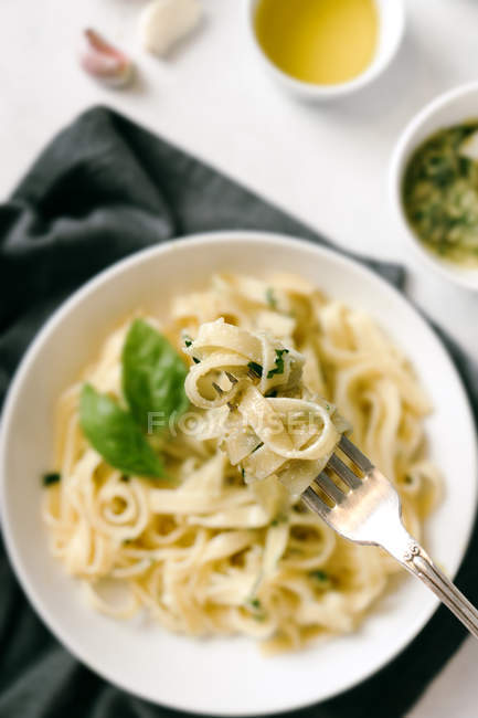 Placa servida de pasta de pesto y tenedor junto al bol de salsa en la mesa. — Stock Photo