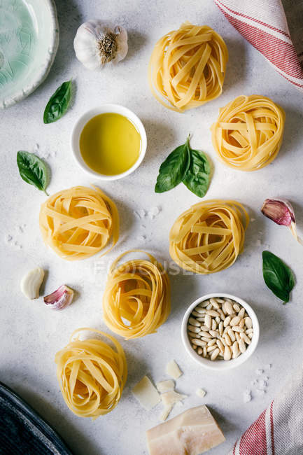 Vista dall'alto di pasta cruda e pinoli con aglio ed erbe aromatiche su tavolo da cucina bianco — Foto stock