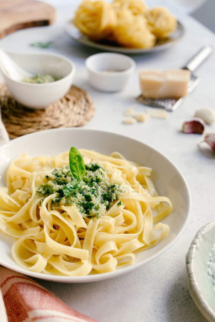 Served plate of pesto pasta next to bowl of sauce on table — Stock Photo