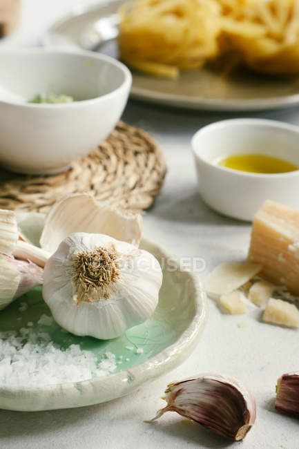 Raw garlic cloves on plate next to cheese and oil on kitchen table — Stock Photo