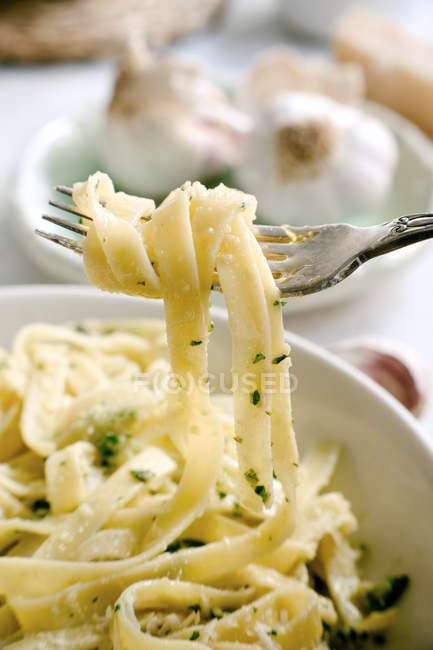 Закрытие вилки вкусной пастой с травами и сыром, подаваемой на тарелке на кухонном столе — стоковое фото