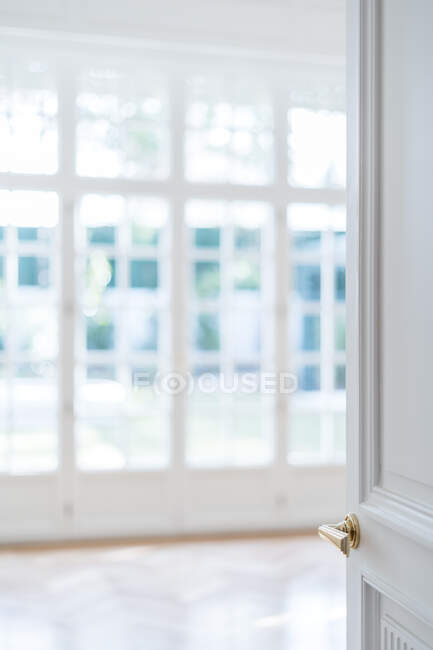 Porta branca aberta com alça dourada em interior minimalista claro no fundo embaçado — Fotografia de Stock