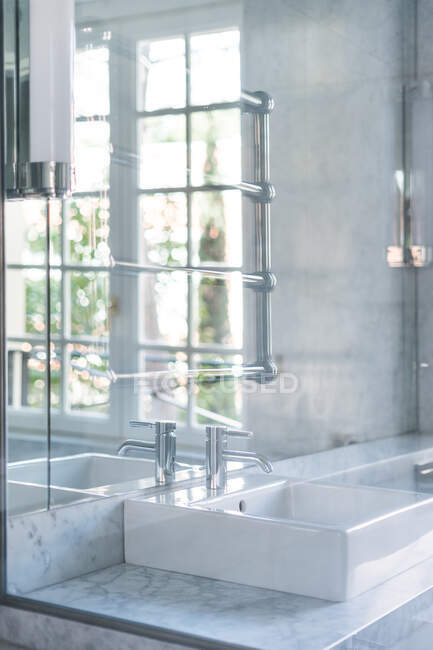 Lavabo carré blanc et robinet en acier dans une salle de bain chic à la lumière du jour — Photo de stock