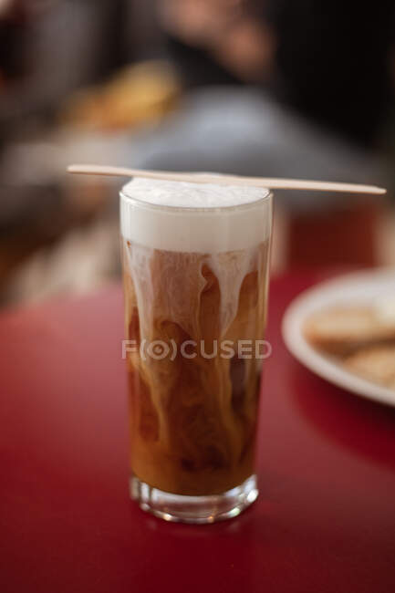 Braunes Gebräu mit Milchschaum in hohem Glas auf rotem Tisch serviert — Stockfoto
