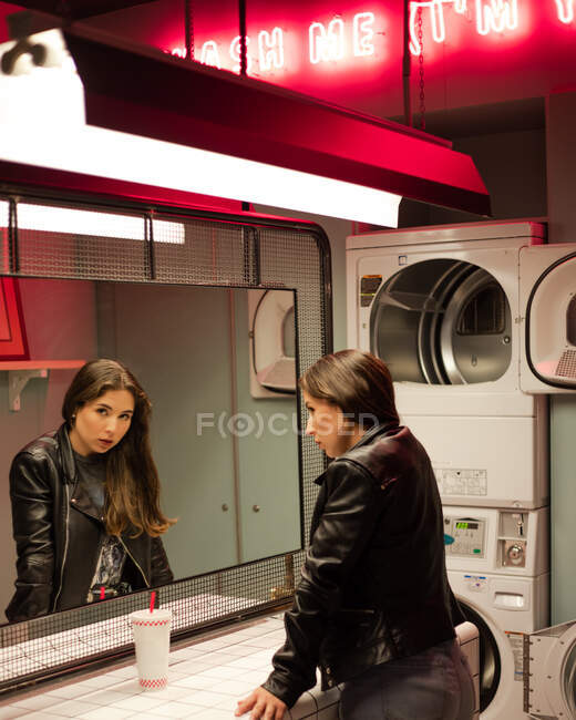 Carefree woman with drink in modern laundromat — Stock Photo