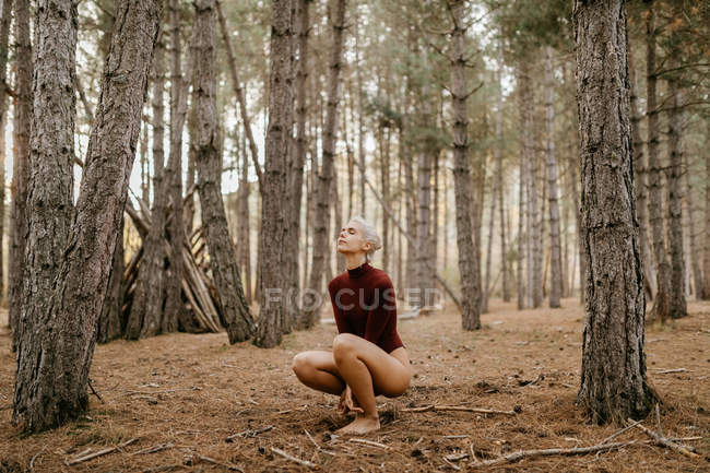 Beautiful modern woman resting barefoot in evergreen forest — Stock Photo