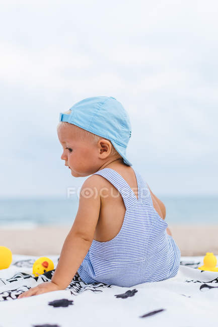 Bebê com um boné na praia ao lado de seus patos de borracha — Fotografia de Stock