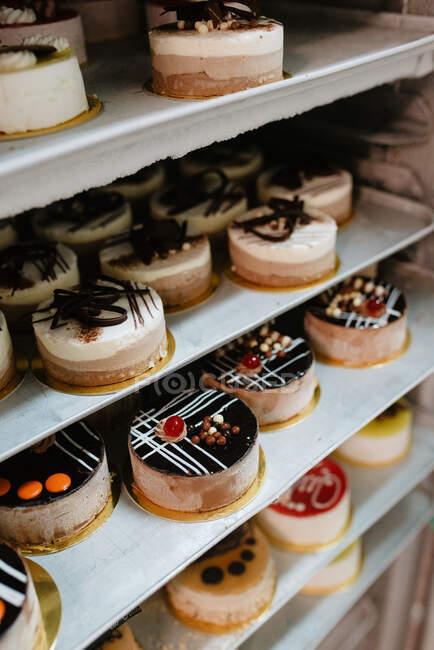 Pequenos bolos envidraçados saborosos colocados em prateleiras de metal na cozinha da padaria — Fotografia de Stock