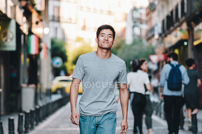Contenuto asiatico uomo in t camicia passeggiando lungo urbano estate strada — Foto stock