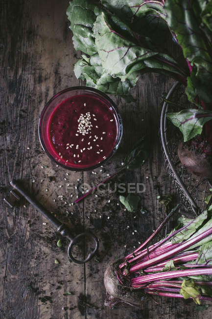Стекло органического вкусного свекловичного смузи с кунжутом на деревянном столе с сырыми овощами и винтажным ключом — стоковое фото