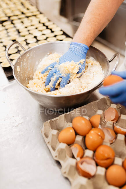 Crop confectioner in gloves and uniform mixing and kneading soft fresh dough while preparing pastry in bakery — Stock Photo