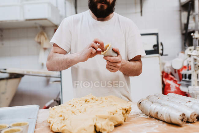 From anonymous confectioner putting fresh soft dough in small cup over table in bakery kitchen — Stock Photo