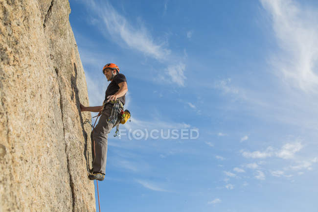 De baixo do homem escalando uma rocha na natureza com equipamento de escalada — Fotografia de Stock