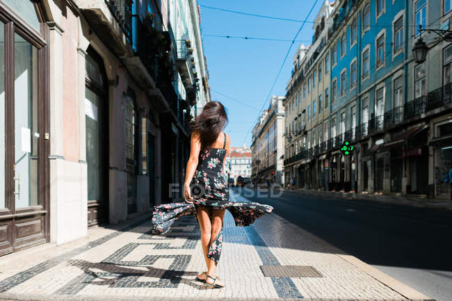 Вид ззаду жінки в довгій сукні, що обертається під час прогулянки по міській літній вулиці — стокове фото