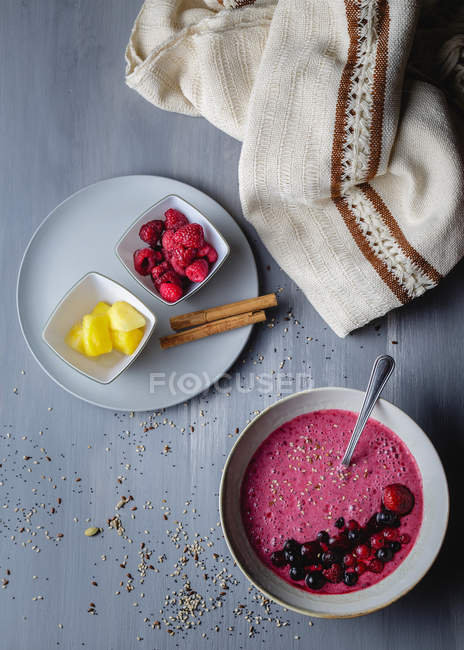 Top view of colorful smoothie bowl with fresh berries and sesame next to plate with raspberries and cut mango — Stock Photo