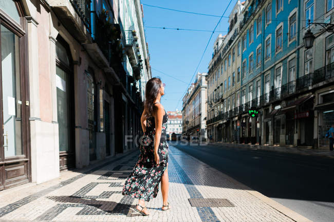 Вид ззаду жінки в довгій сукні, що обертається під час прогулянки по міській літній вулиці — стокове фото