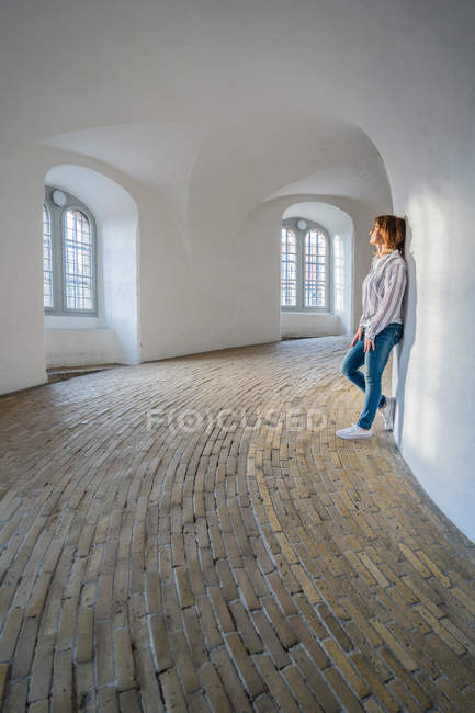Casual woman leaning on wall in spacious gallery with windows — Stock Photo