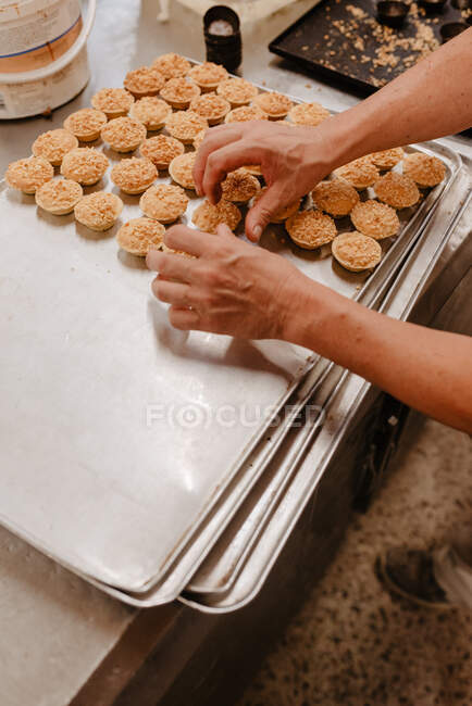 From above unrecognizable confectioner putting small yummy pastry on metal tray while working in bakery — Stock Photo