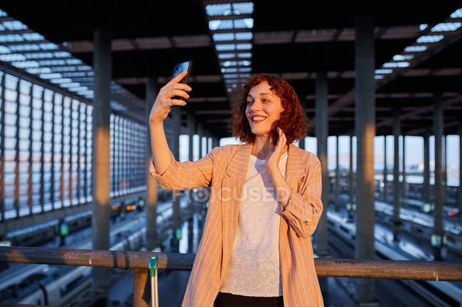 Улыбающаяся молодая женщина делает селфи на станции — стоковое фото