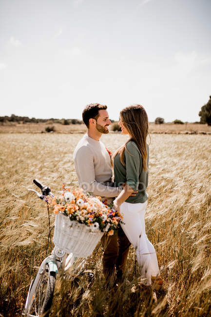 Side view of amorous couple posturing near vintage bike on wheat field in summertime — Stock Photo