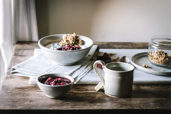 Delicious breakfast bowl with berries, quinoa, rice and groats near tea cup and newspaper — Stock Photo