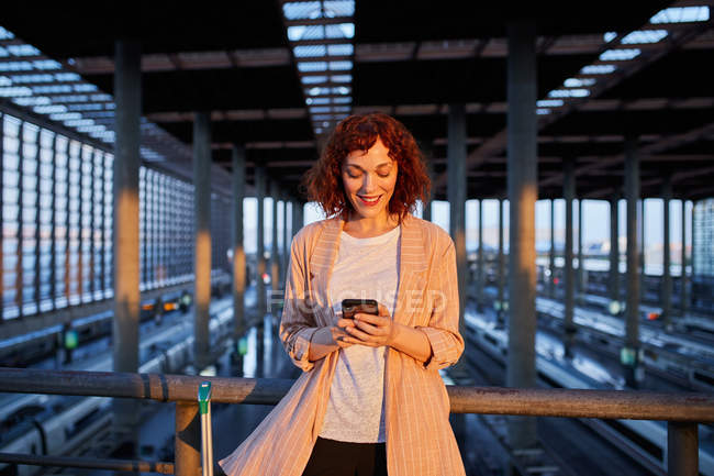 Sorrindo jovem mulher que navega telefone na estação — Fotografia de Stock