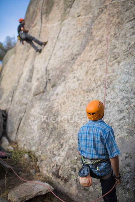 Aventureros escalando montaña usando arnés de seguridad contra pintoresco paisaje - foto de stock