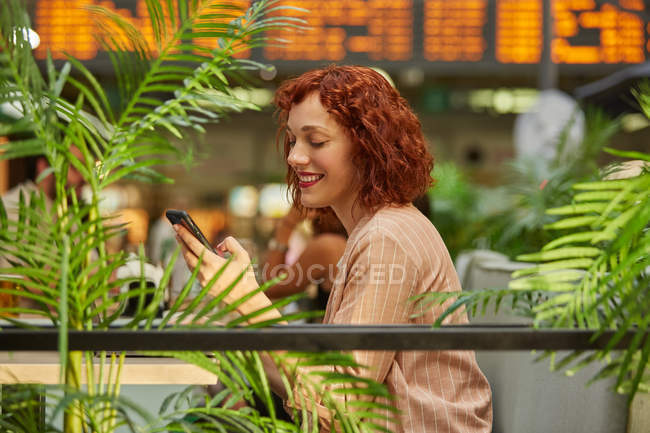 Cheerful young woman working on laptop in cafe and browsing phone — Stock Photo