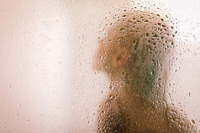 Vista laterale della giovane femmina che si fa la doccia dietro la parete divisoria trasparente bagnata in bagno — Foto stock