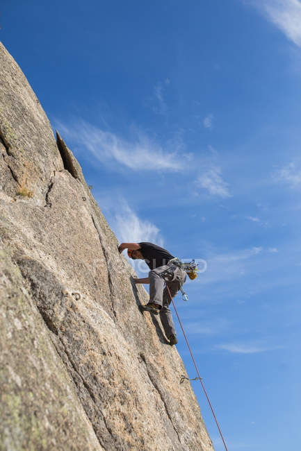 Desde abajo el hombre escalando una roca en la naturaleza con equipo de escalada - foto de stock